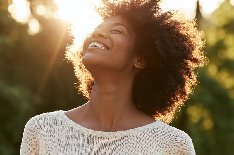 Young black woman laughing with head tilted back in sunlight outdoors
