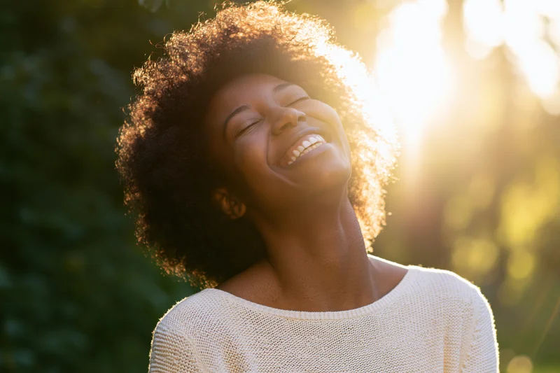 Young black woman laughing with eyes closed in sunlight outdoors