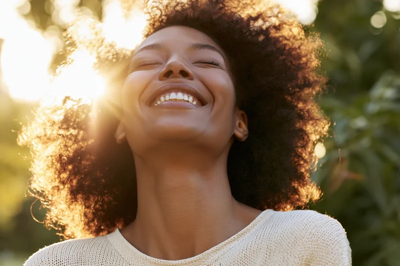 Young black woman smiling with eyes closed, head tilted back in sunlight outdoors