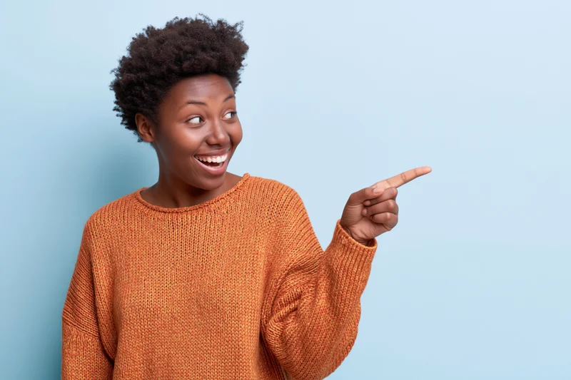 Young black woman smiling and pointing to the side against a blue background