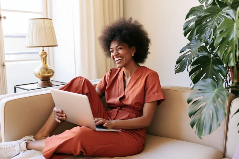 Woman laughing while using laptop on sofa at home
