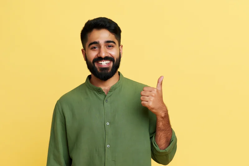 Young indian man smiling and giving thumbs up against yellow background