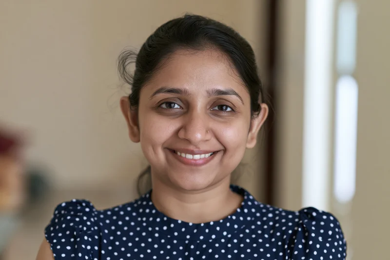Young indian woman smiling warmly at camera in indoor setting wearing navy blue polka dot blouse