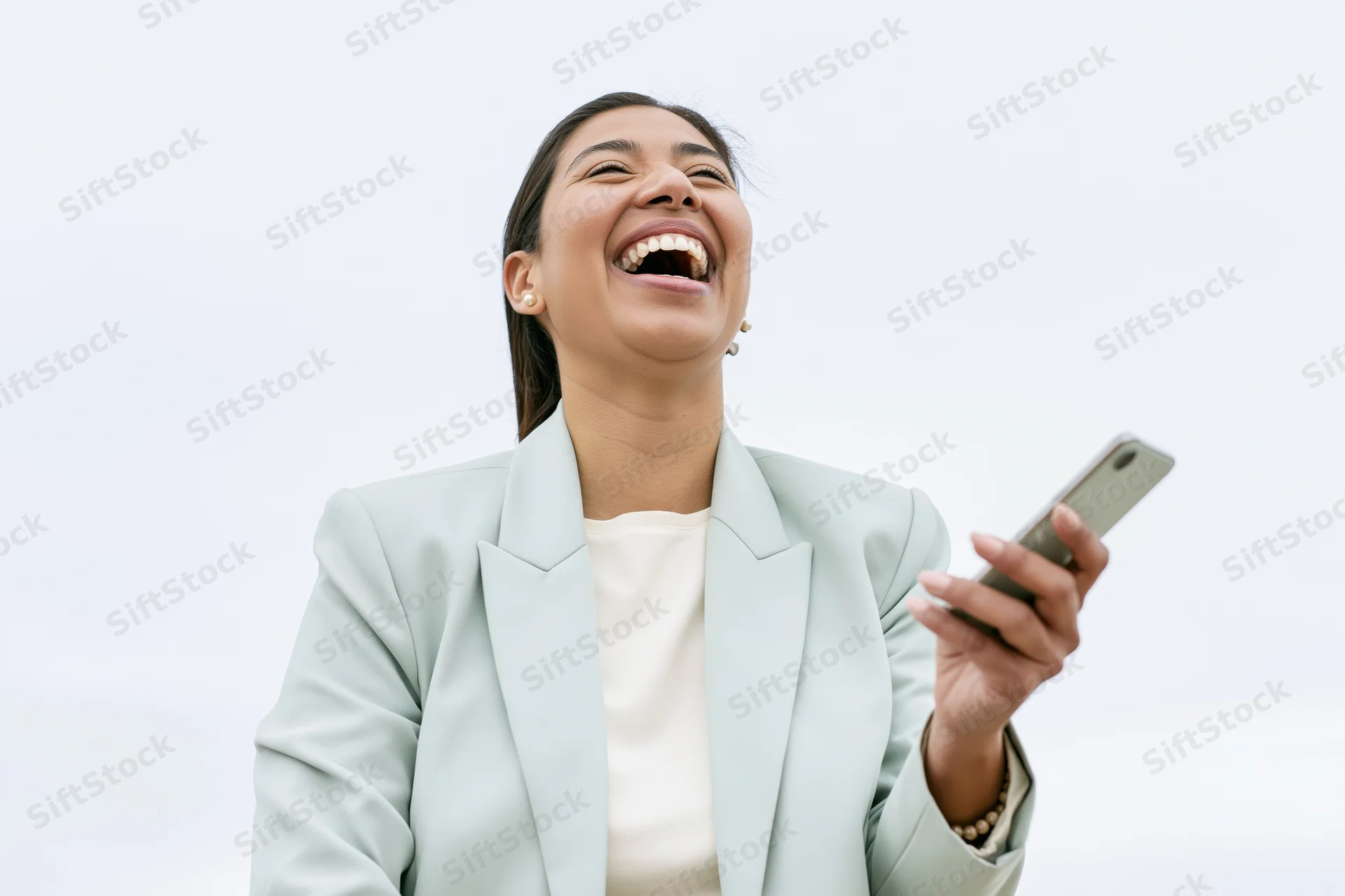 Young latina woman laughing joyfully while holding smartphone outdoors