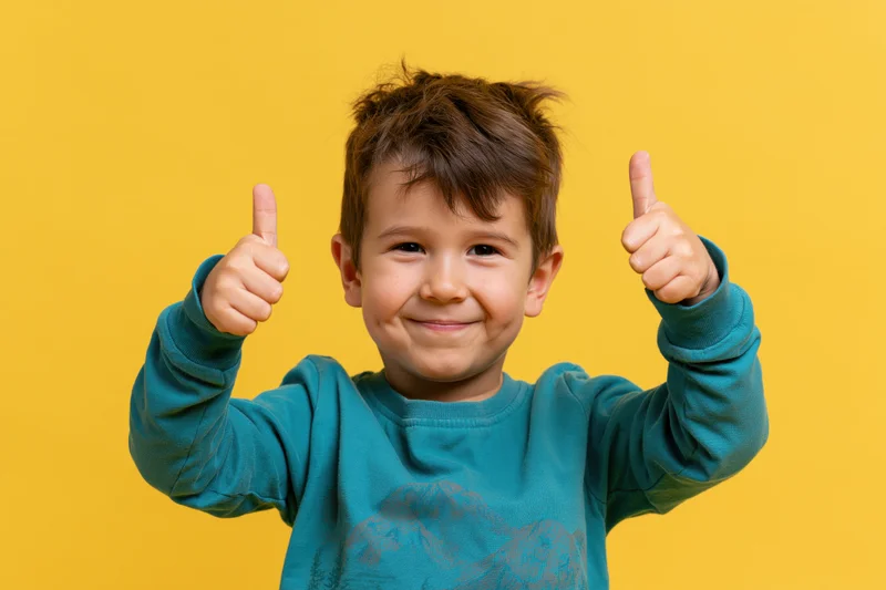 Young boy giving double thumbs-up against yellow background