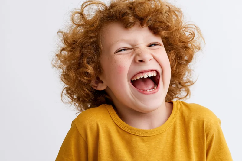 Young child with voluminous curly light-brown hair laughing in a studio portrait