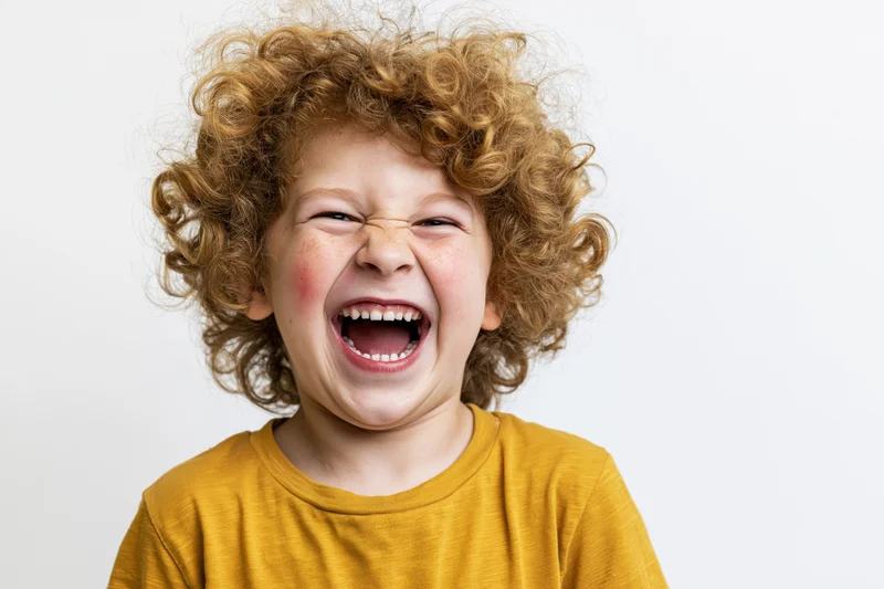 Young boy with voluminous curly light-brown hair laughing joyfully in a studio portrait