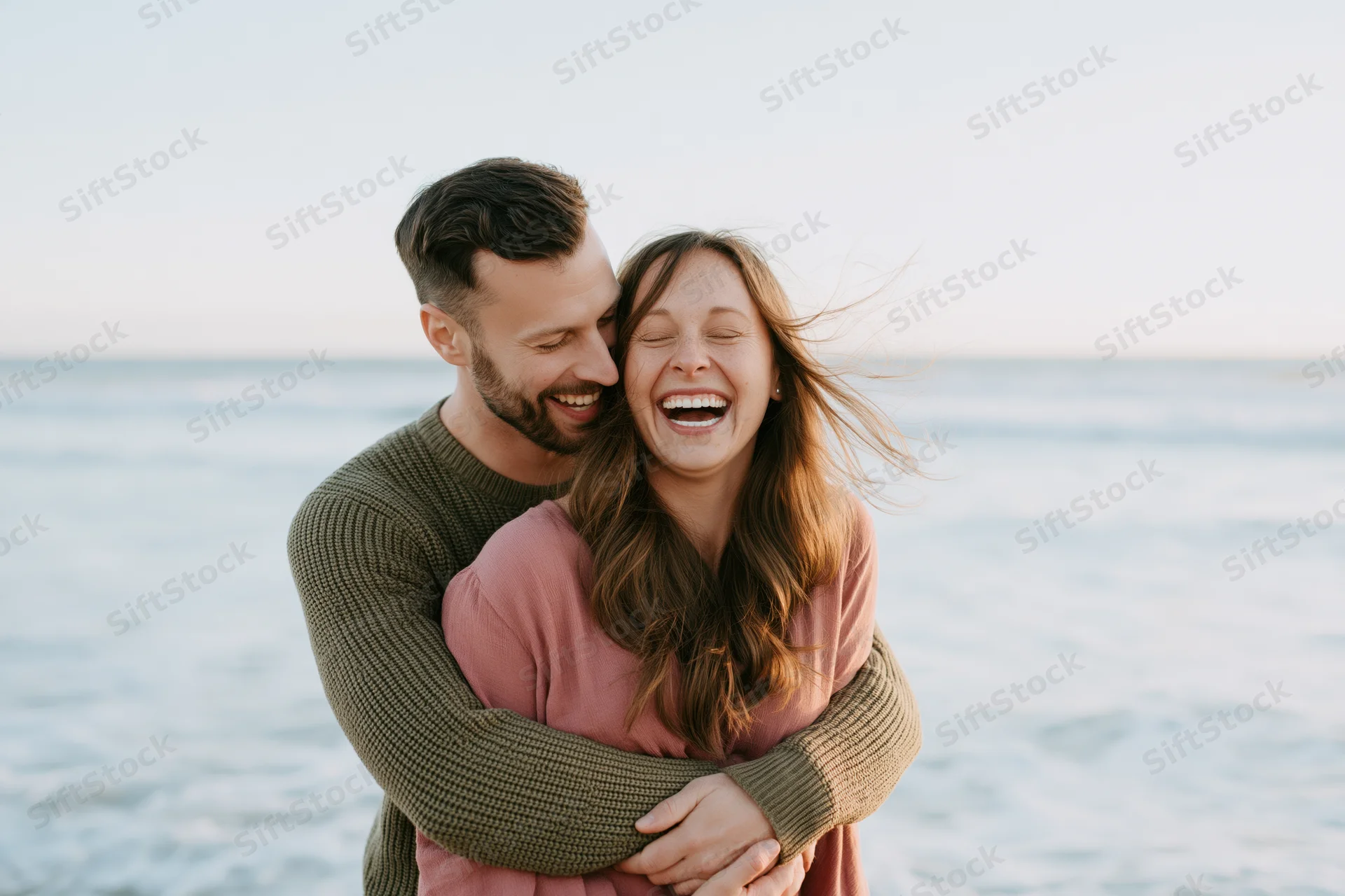Man hugging woman from behind as she laughs on a beach