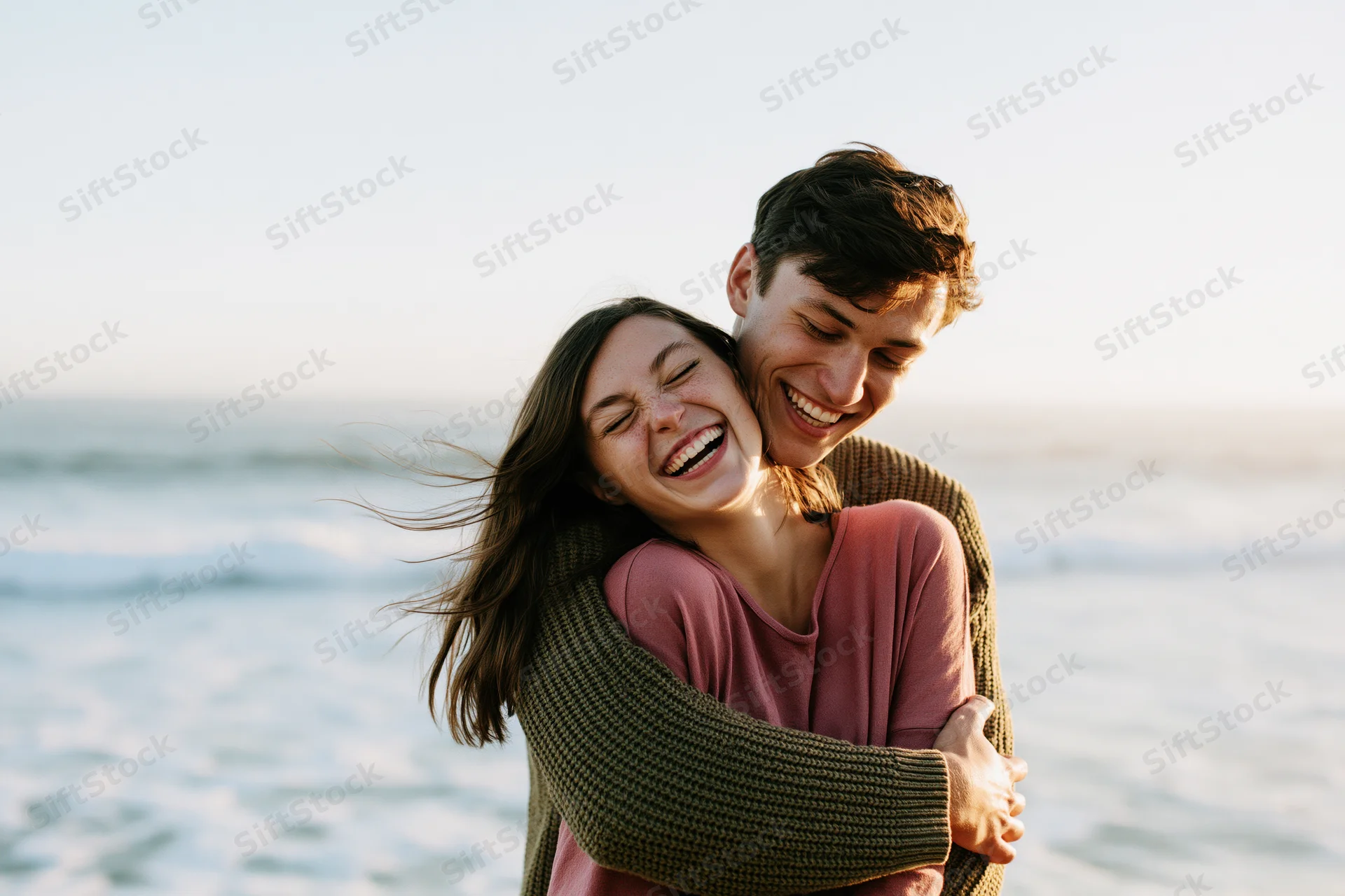 Young couple embracing on a beach with ocean waves behind them