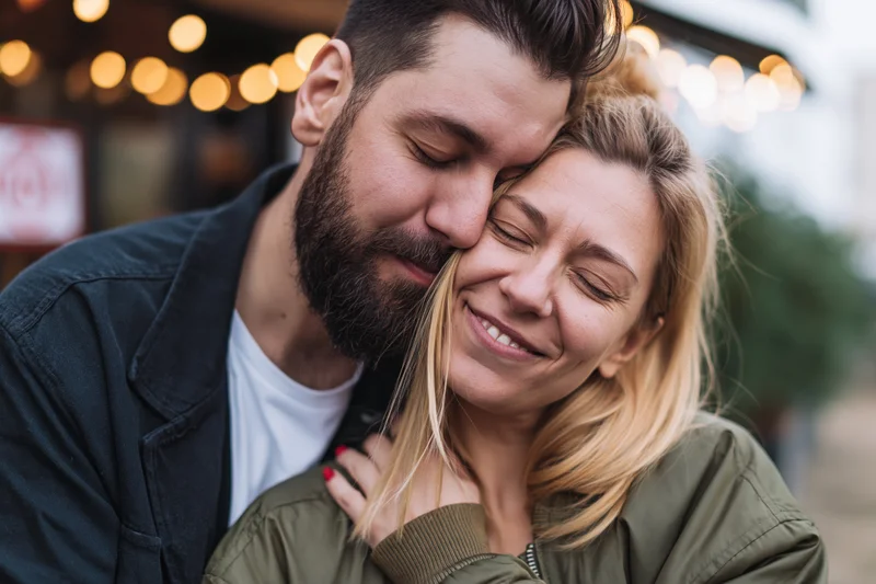 Couple embracing closely on a city street at evening with warm bokeh lights in background