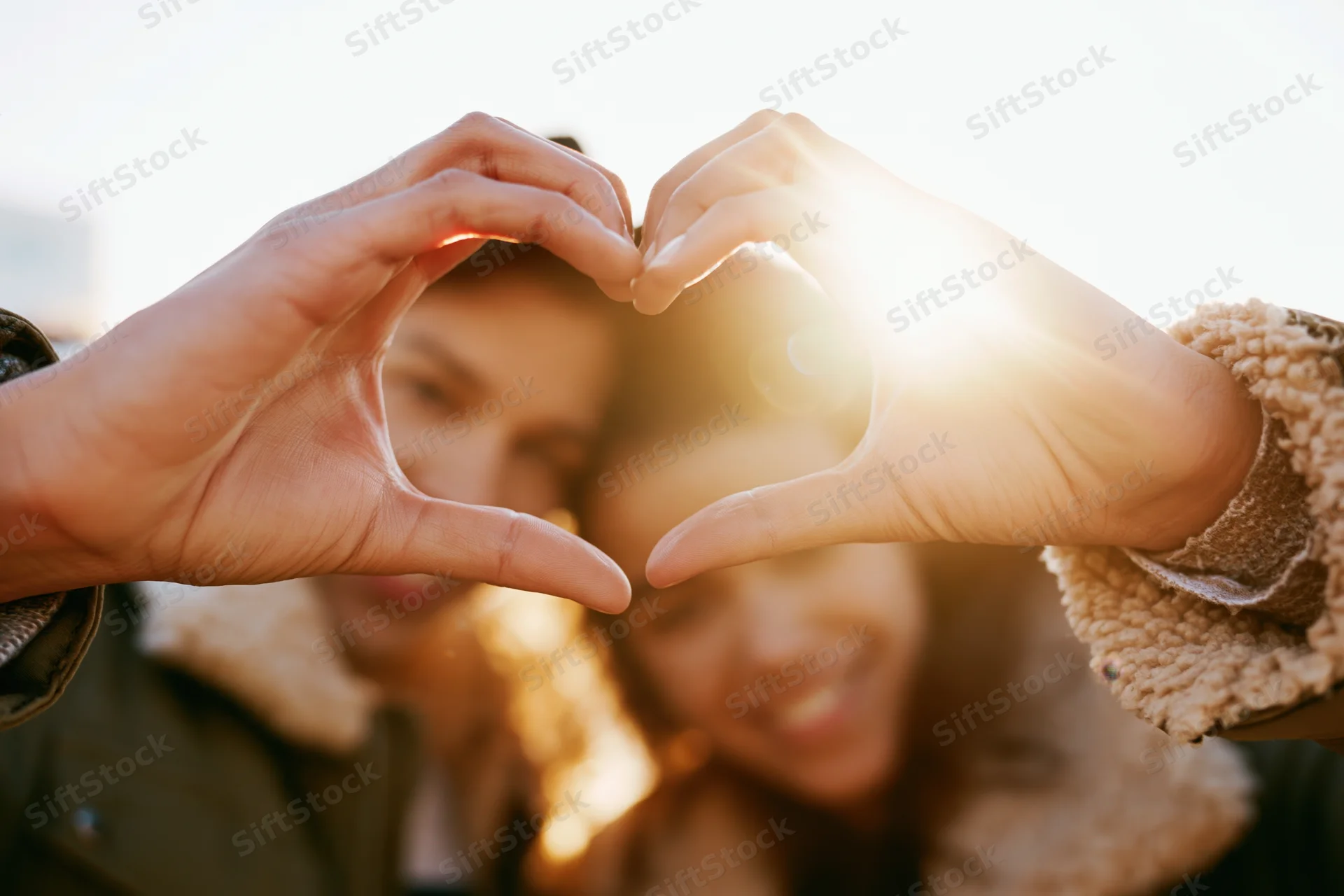 Young couple forming heart shape with hands outdoors in sunlight