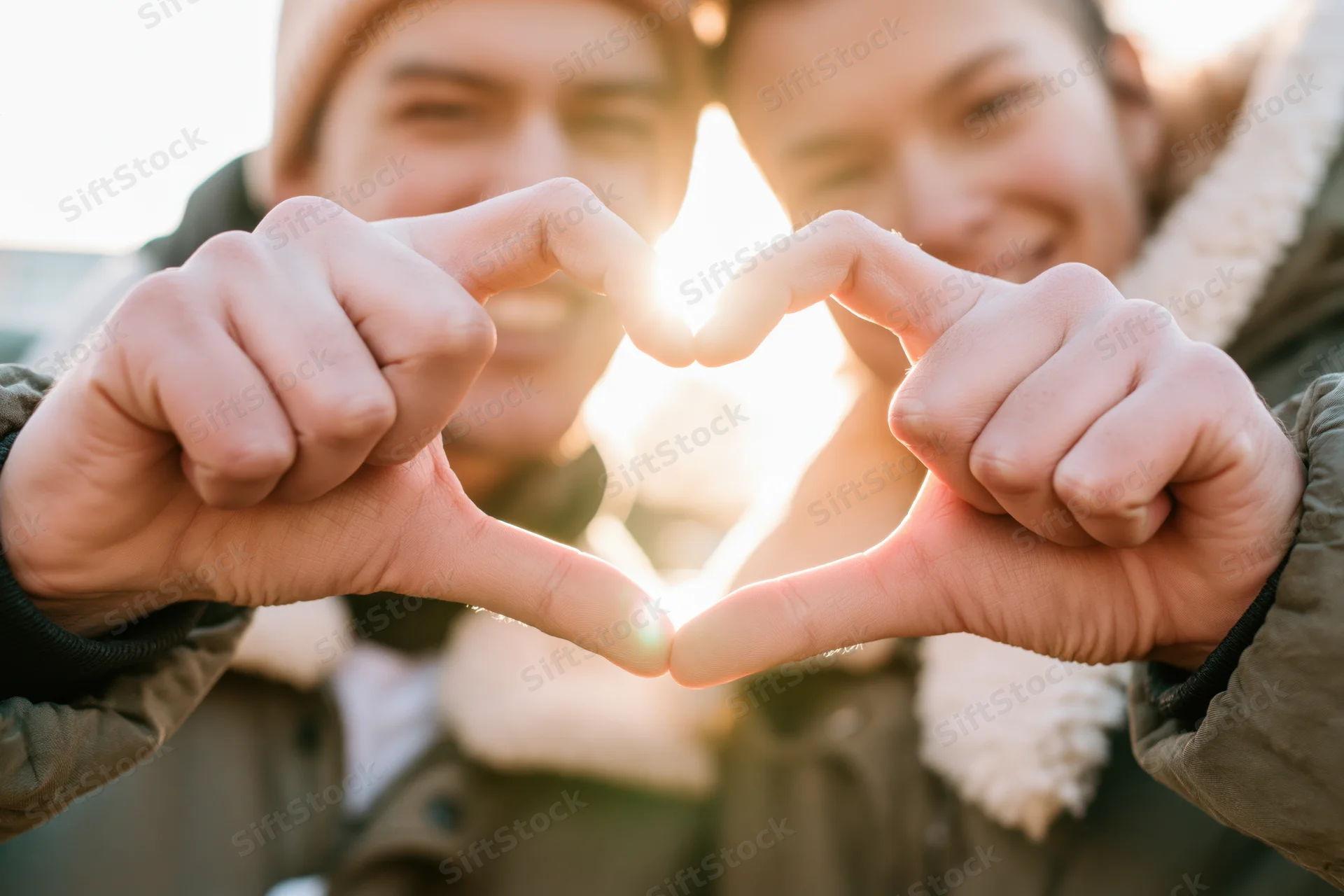 Young couple forming heart shape with hands outdoors in winter sunlight