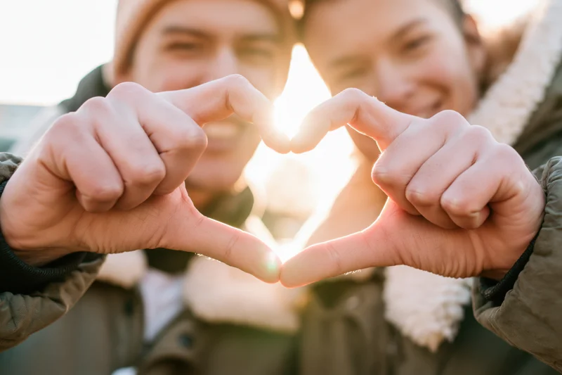 Young couple forming heart shape with hands outdoors in winter sunlight