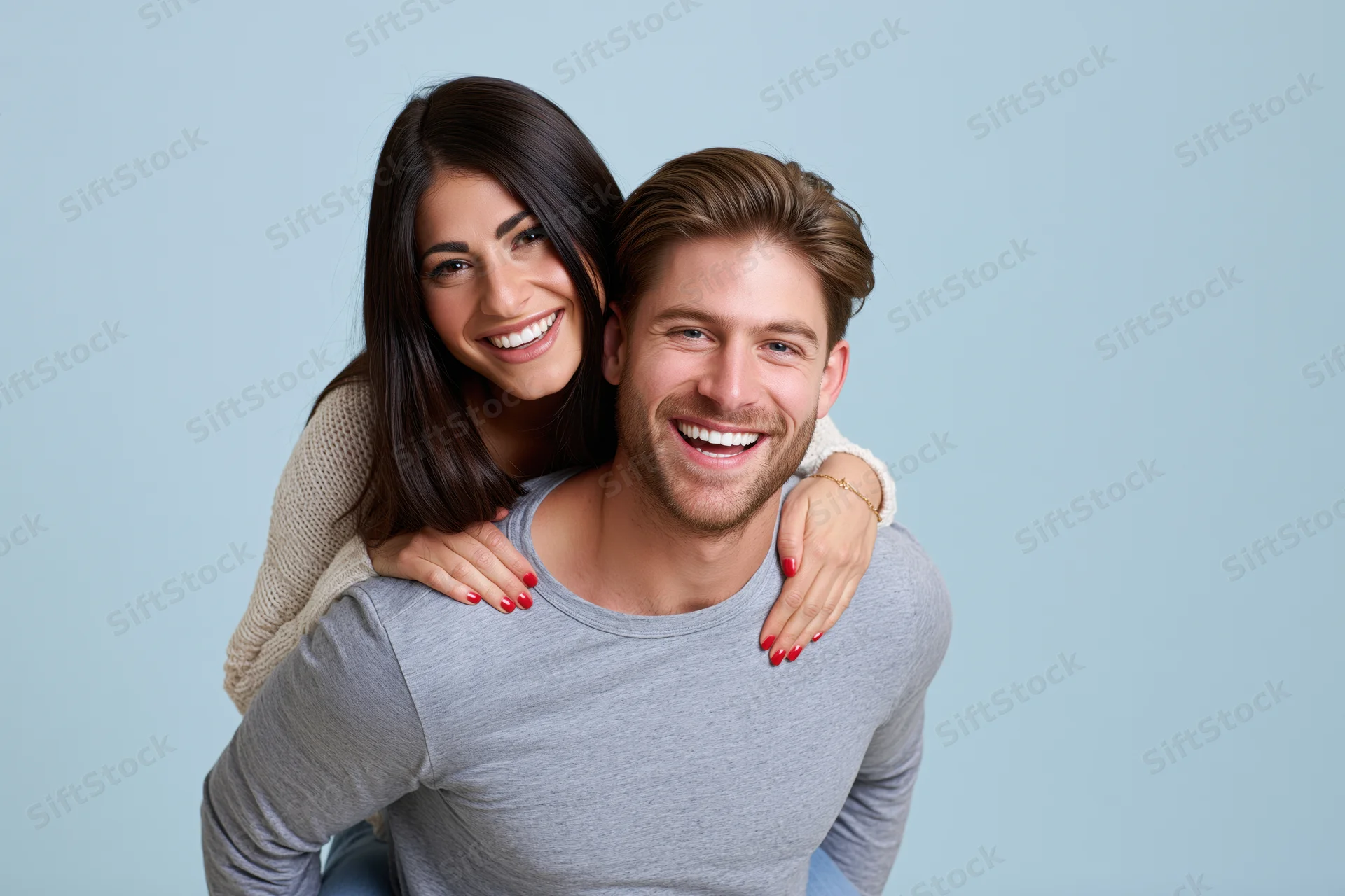 Young couple in piggyback pose smiling at camera against plain blue background