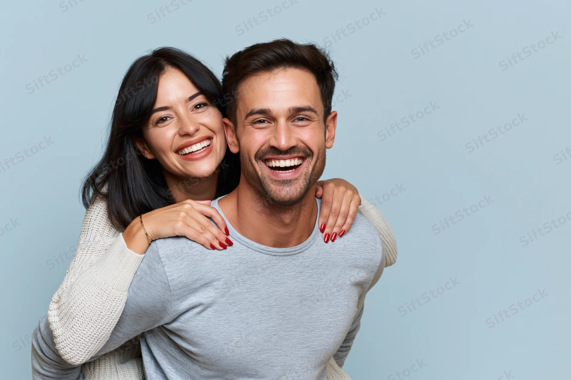 Young couple in piggyback pose smiling against plain blue background
