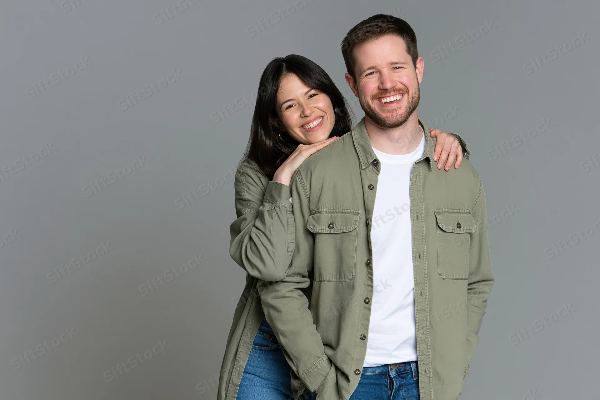 Young couple smiling and embracing closely in casual clothing against a gray studio background