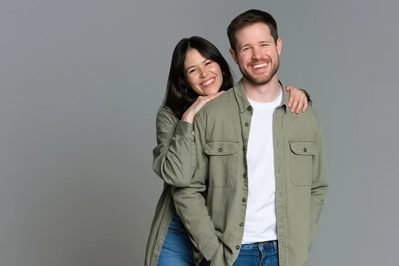 Young couple smiling and embracing closely in casual clothing against a gray studio background
