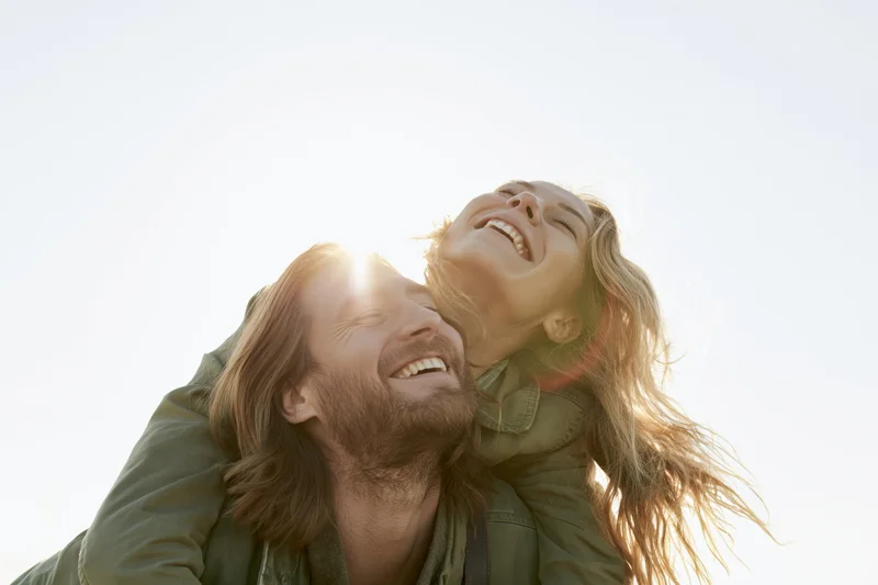 Woman laughing while piggybacking on man outdoors in sunlight