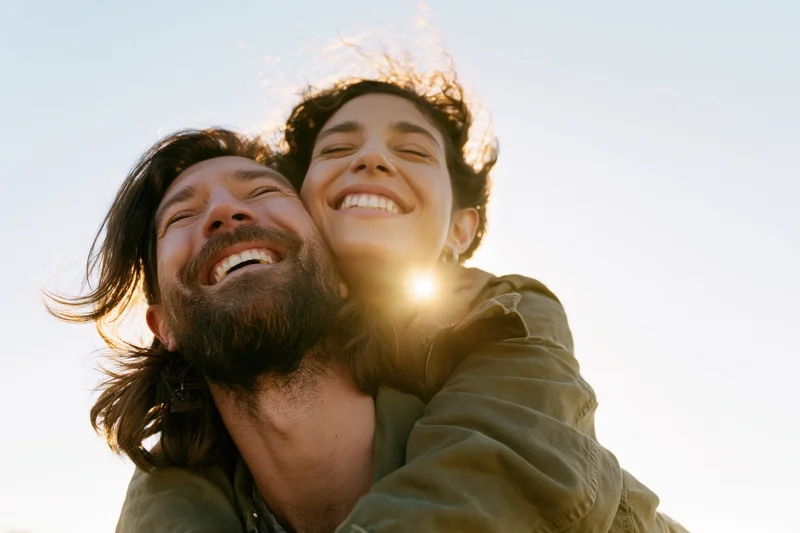 Woman riding piggyback on man outdoors laughing in sunlight