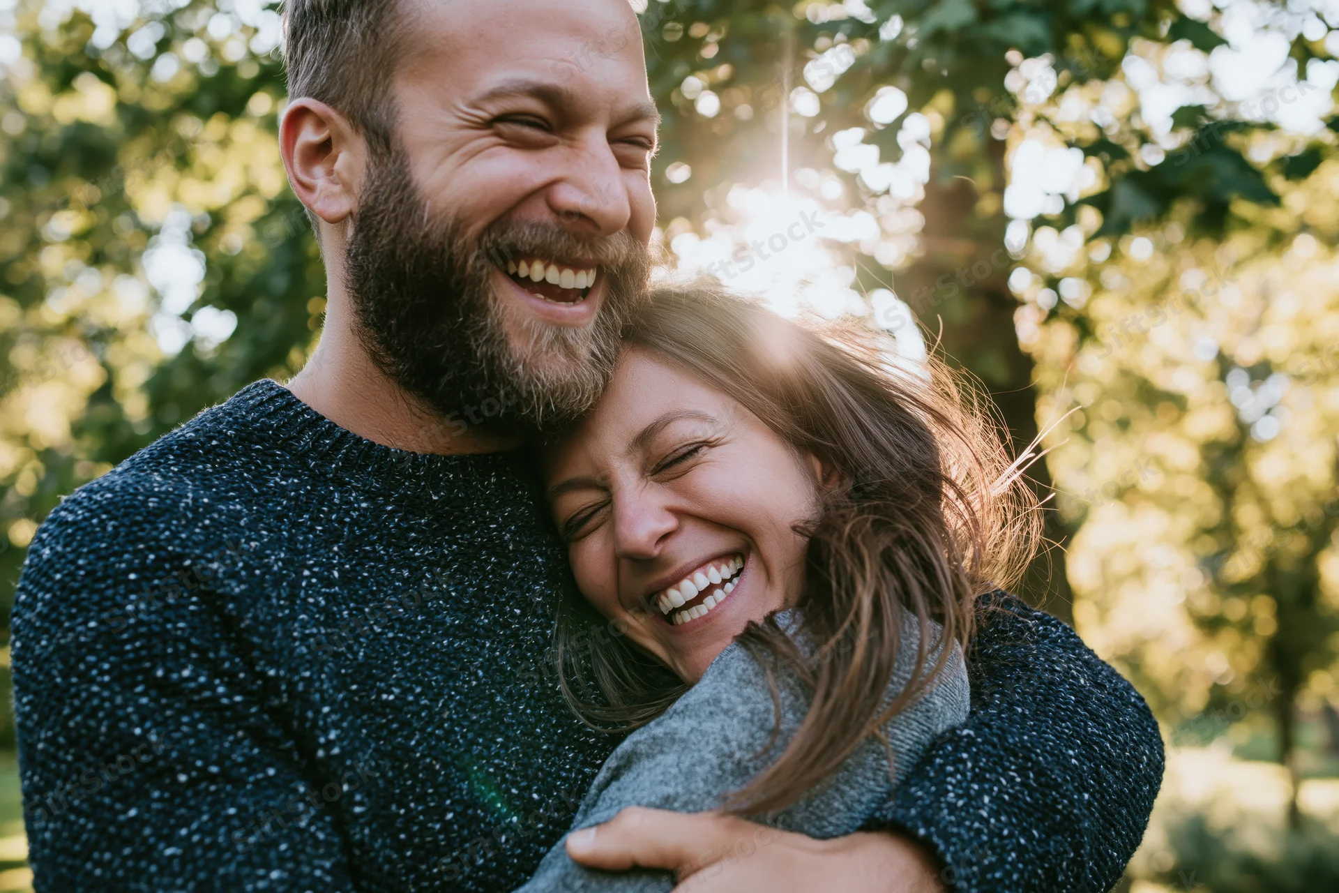 Couple laughing and hugging in a sunlit park surrounded by trees