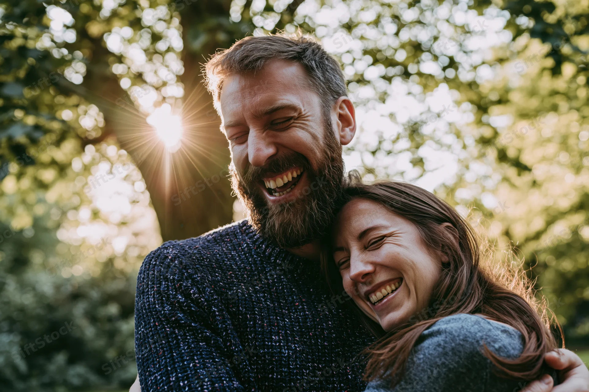 Laughing couple embracing in a park with sunlight filtering through trees
