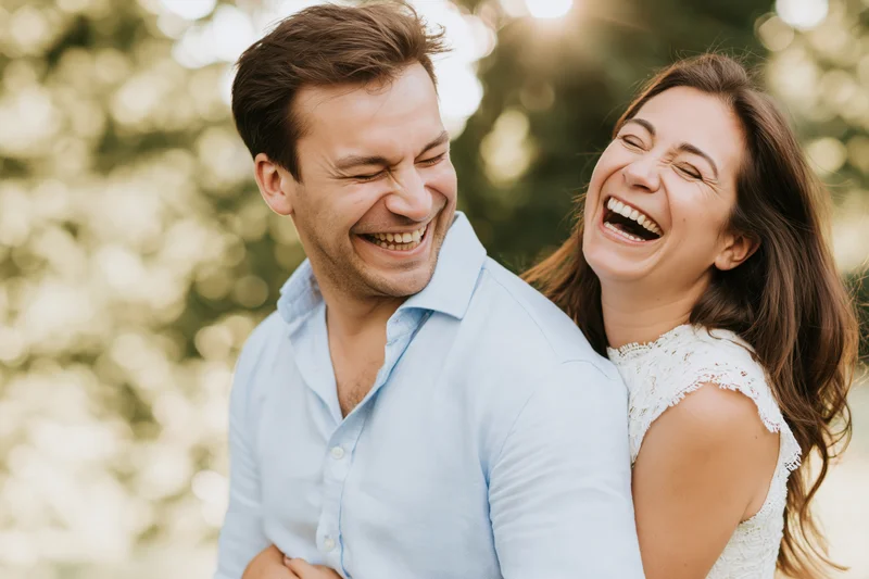 Couple laughing together outdoors in a park with sunlight filtering through trees