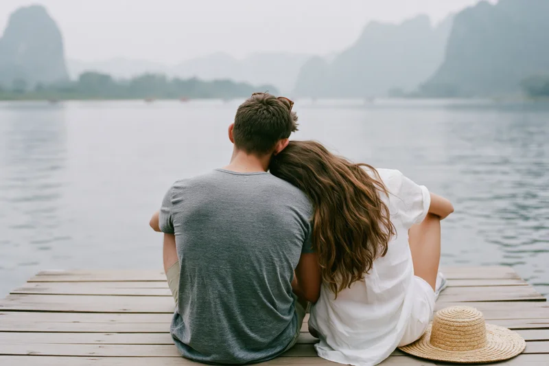 Young couple sitting close together on wooden dock facing lake and mountains