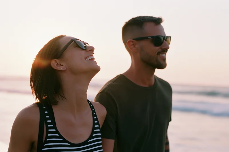 Young couple smiling and wearing sunglasses on a beach at sunset