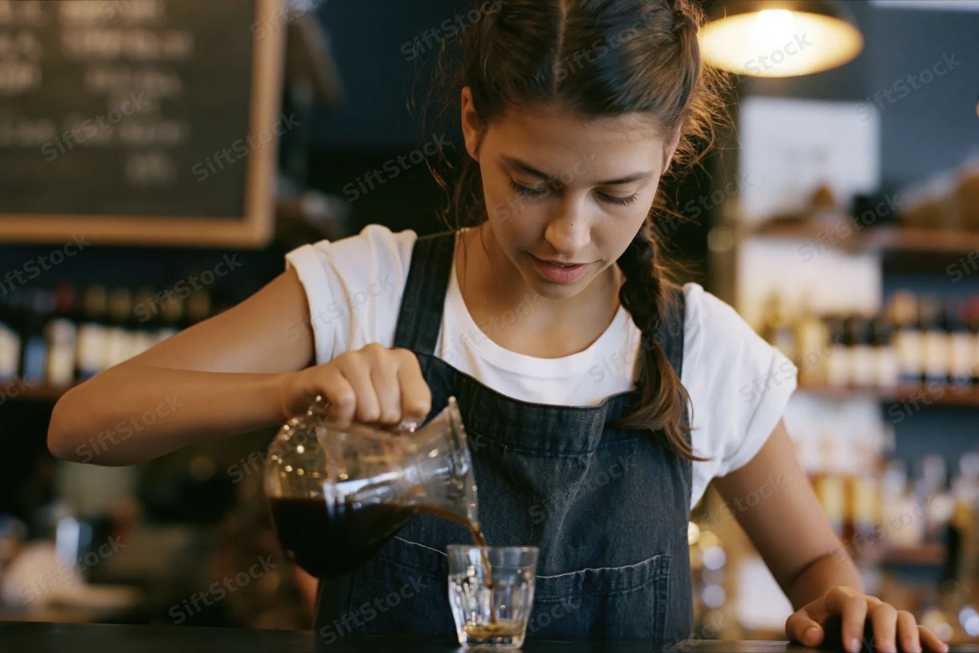 Young woman barista pouring coffee from a glass carafe at a cafe counter