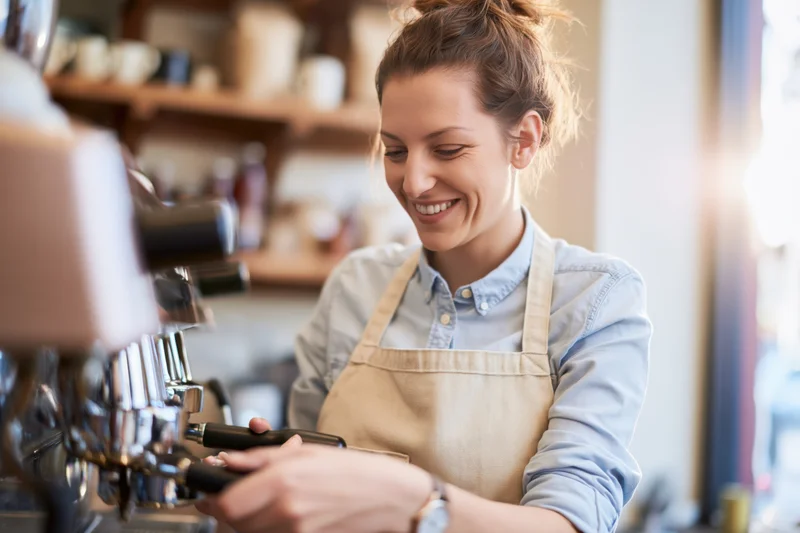 Woman barista smiling while operating espresso machine in cafe interior