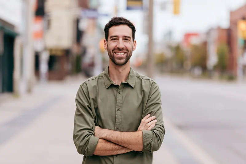 Young man smiling with arms crossed on city sidewalk