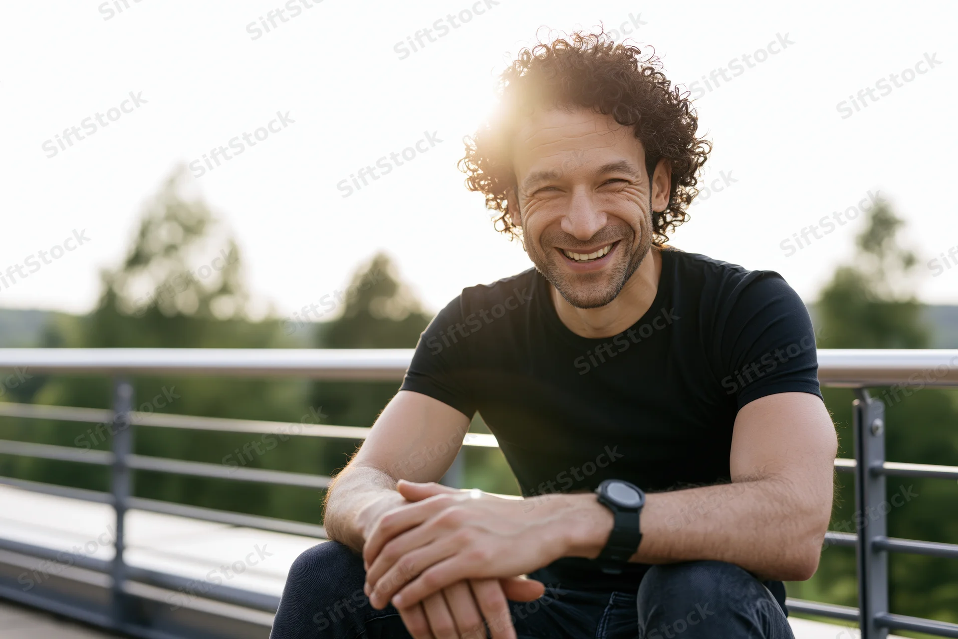 Smiling man with curly hair sitting on outdoor terrace in sunlight