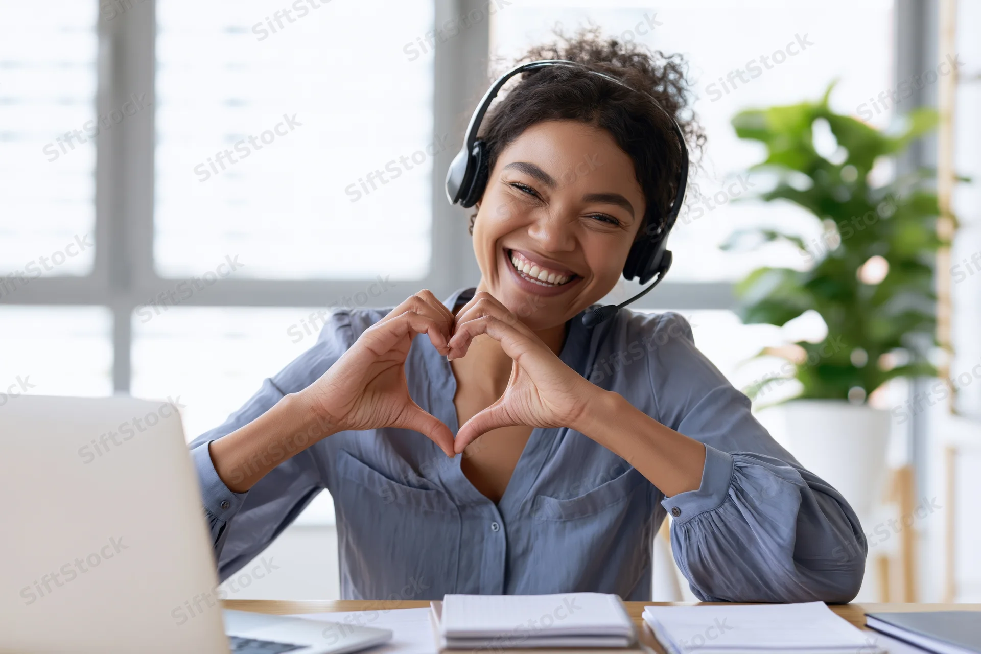 Woman making heart shape with hands while wearing headset at office desk