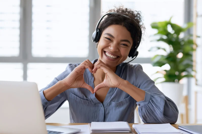 Woman making heart shape with hands while wearing headset at office desk