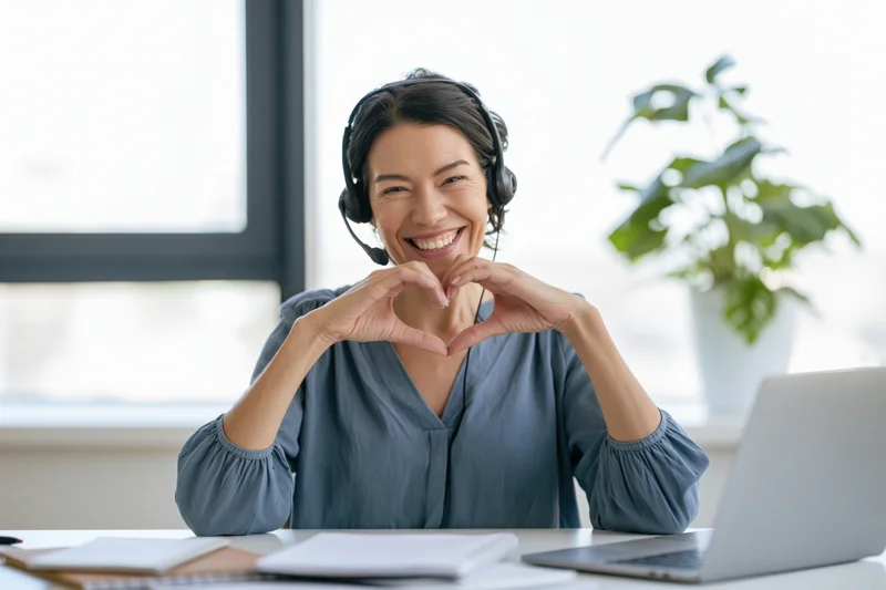Woman call center agent making heart shape with hands at office desk