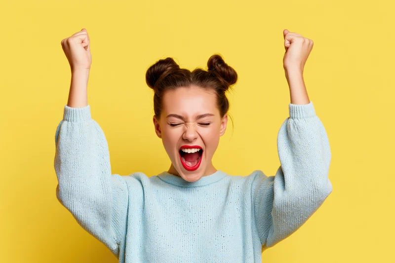 Young woman celebrating with fists raised against yellow background
