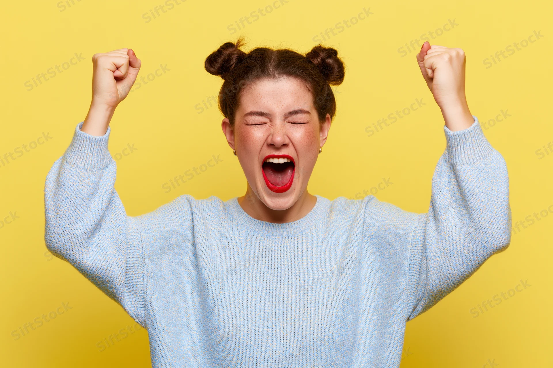 Young woman celebrating with fists raised against yellow background