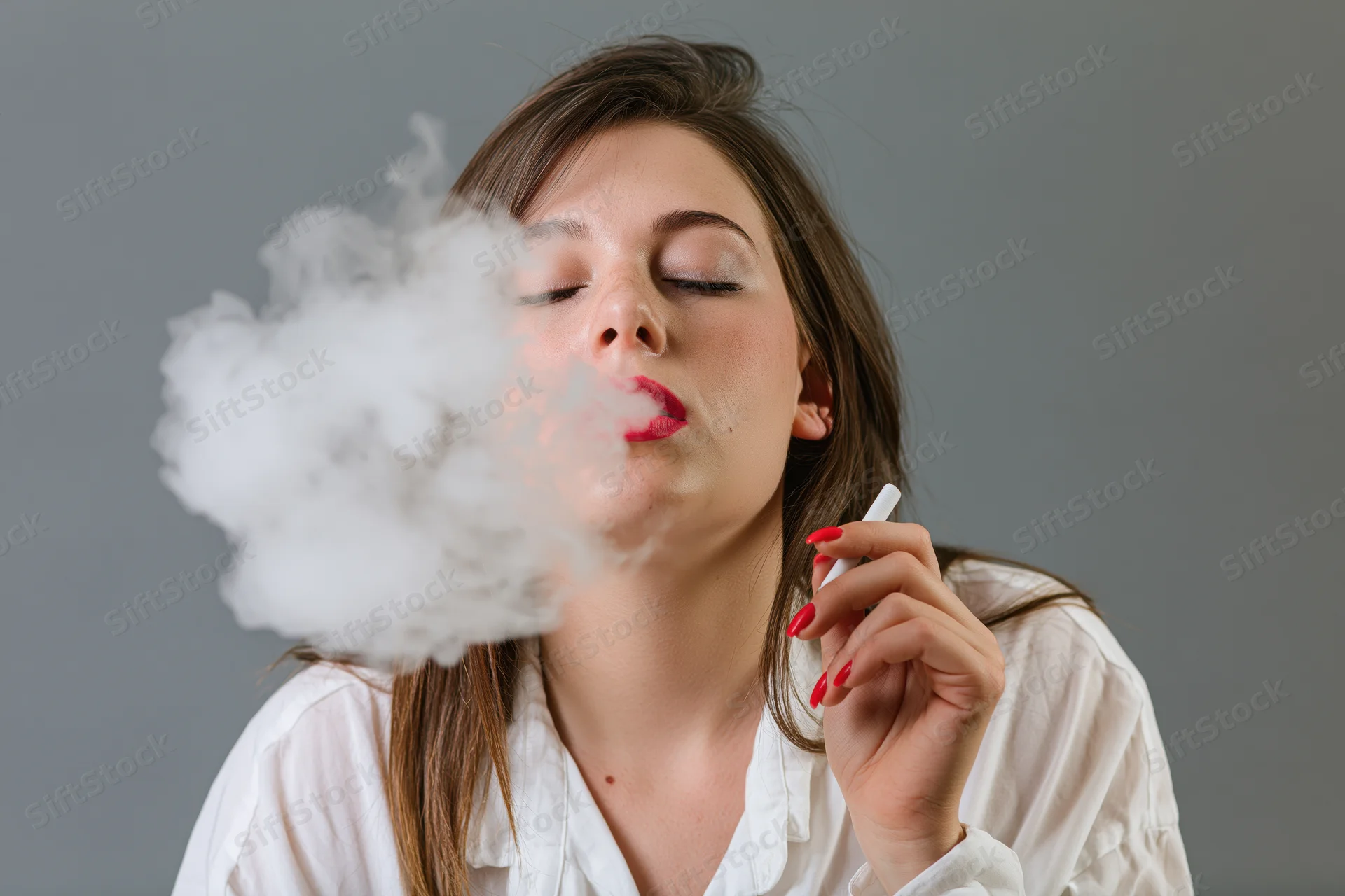 Young woman exhaling thick smoke from a cigarette in a studio setting