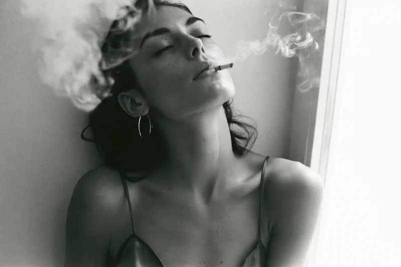 Young woman exhaling cigarette smoke with eyes closed and head tilted back indoors