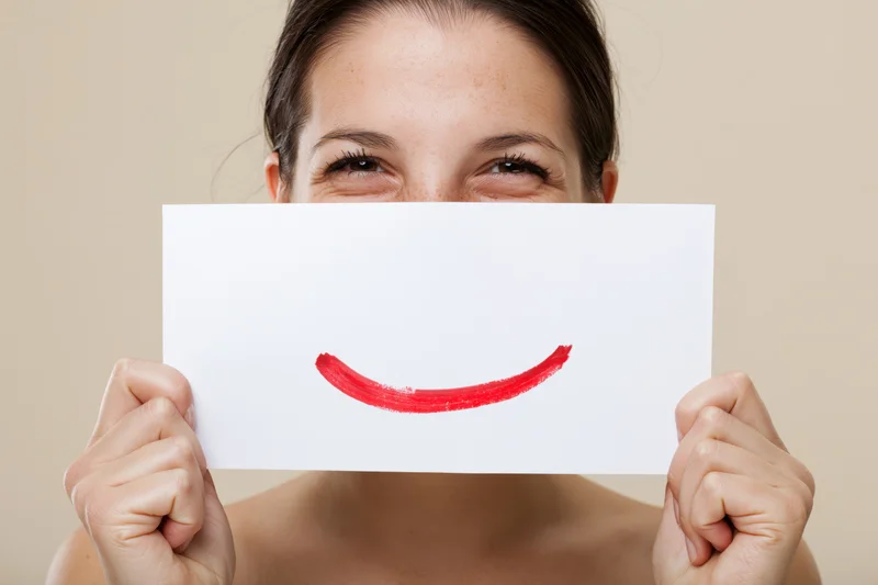 Woman holding white paper with red smile in front of her face