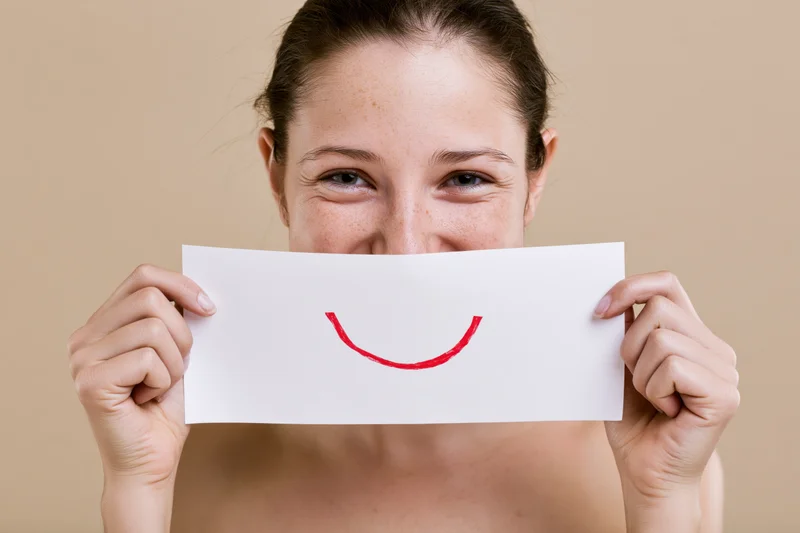 Woman holding white paper with red smile in front of her face, studio shot