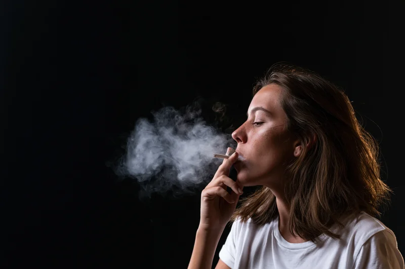 Woman in profile exhaling smoke from a cigarette against a dark background