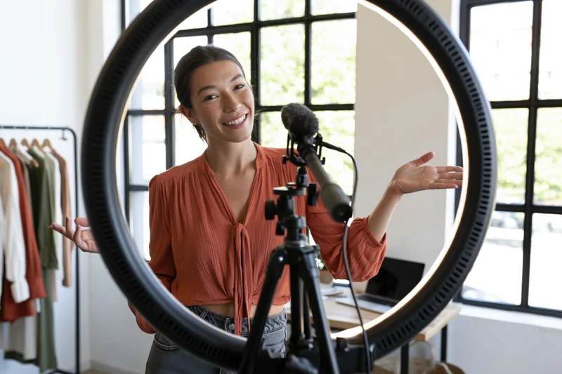 Woman smiling and gesturing while recording a vlog in her home studio with ring light and microphone