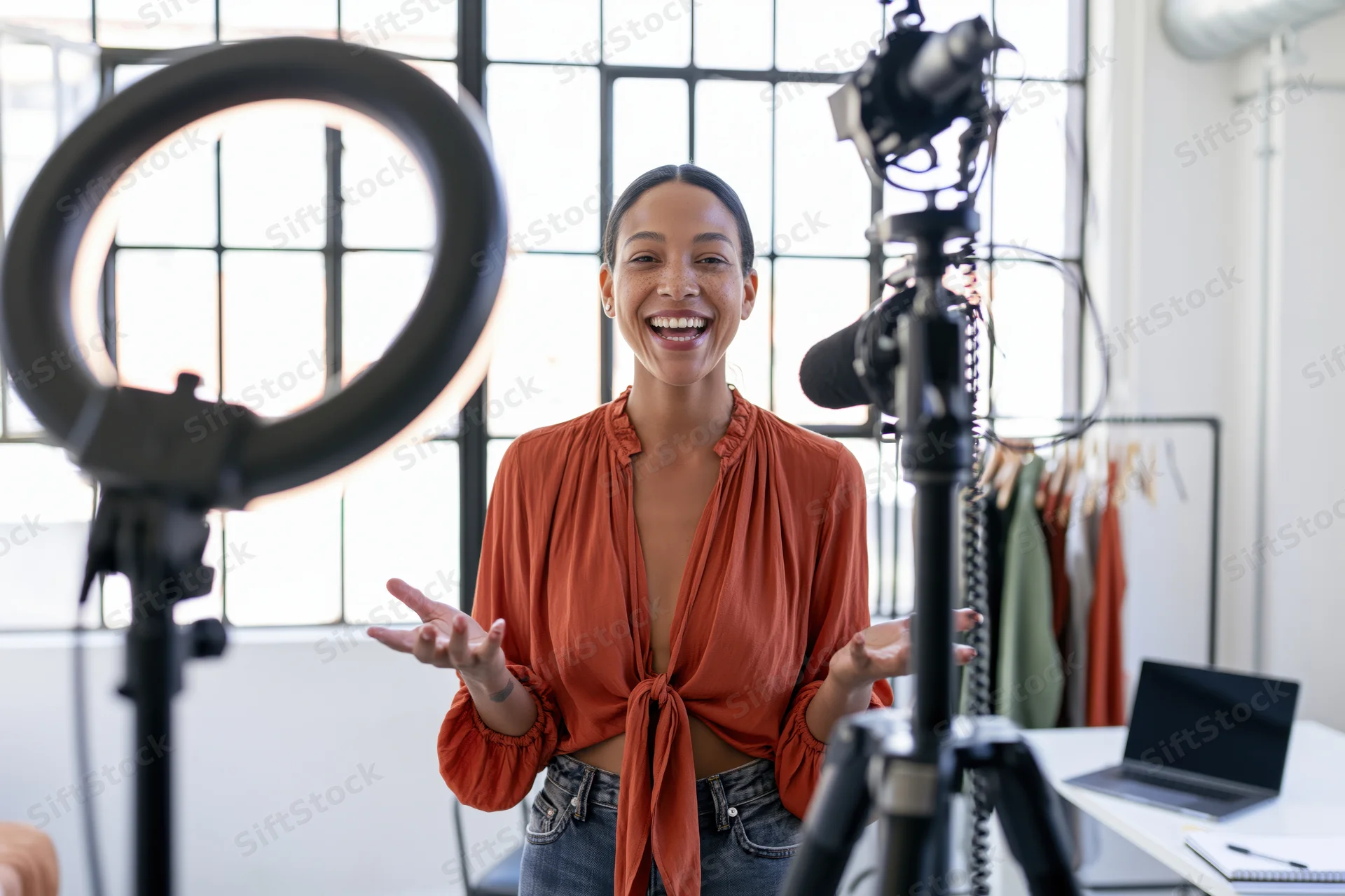 Woman smiling and gesturing while recording a vlog in her home studio with camera and ringlight
