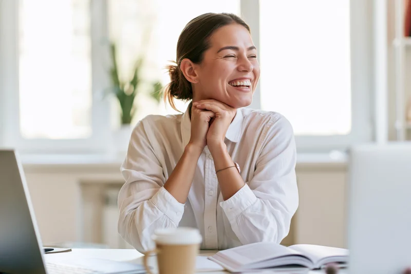Young woman laughing with hands clasped under her chin at office desk