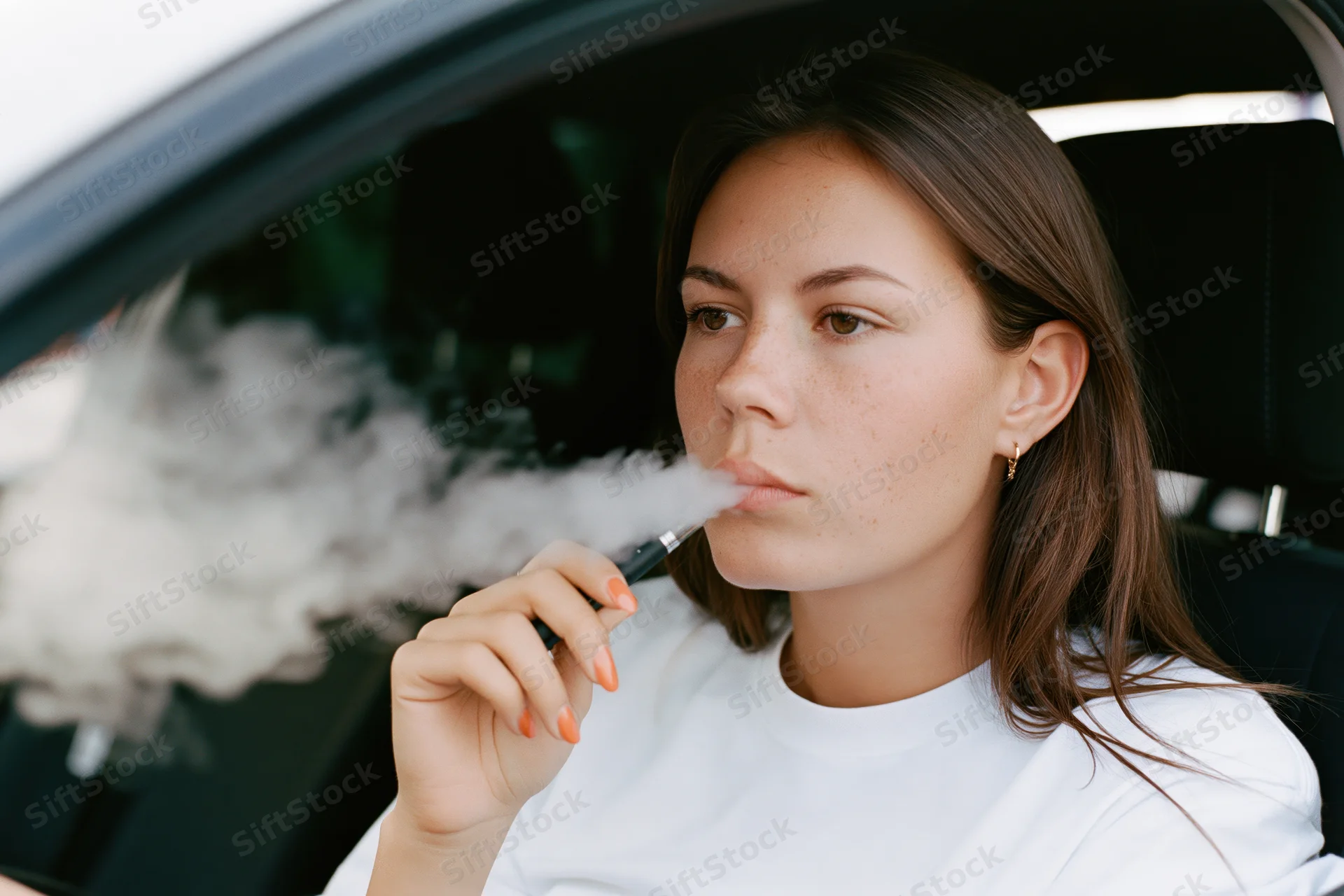 Young woman exhaling vapor while sitting in driver’s seat of a car