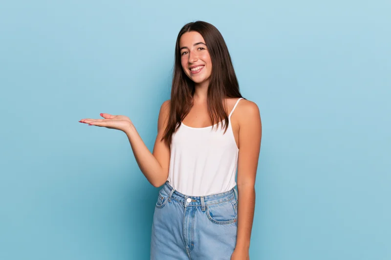 Young woman smiling and presenting an invisible product with open hand against blue background