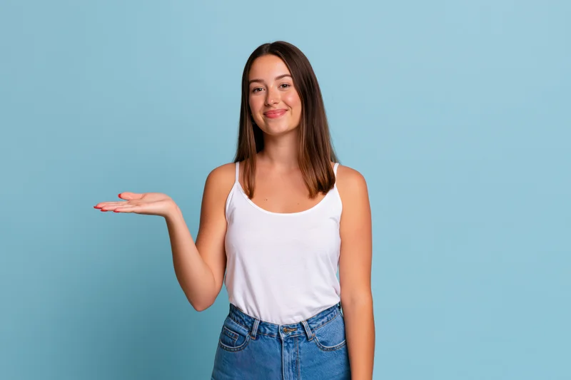 Young woman smiling and presenting an invisible product with open hand against blue background