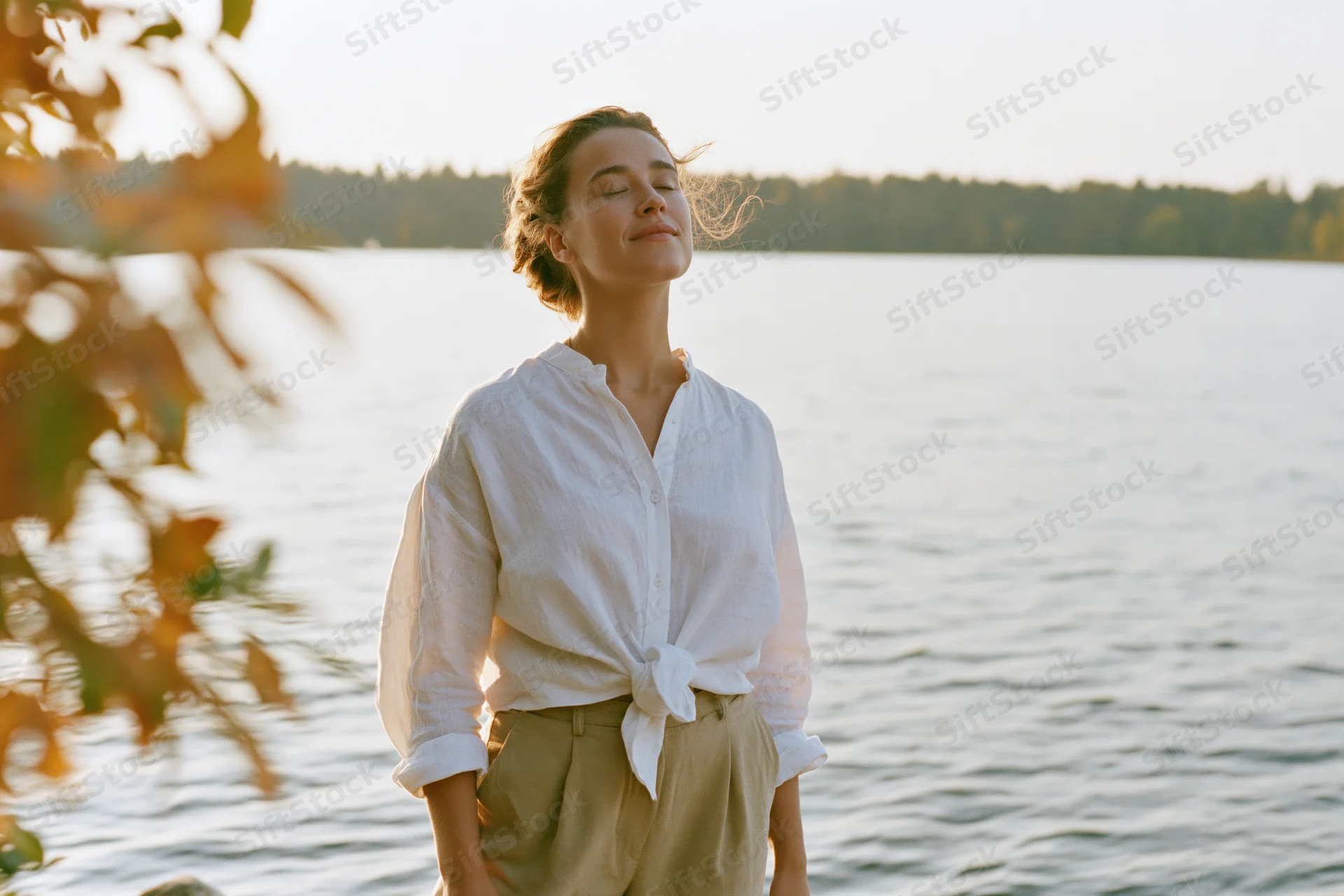 Woman with eyes closed breathing calmly by a lake at golden hour