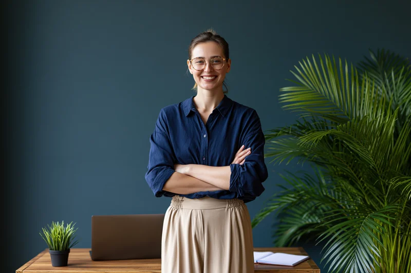 Young woman standing with arms crossed behind a wooden desk in an office setting